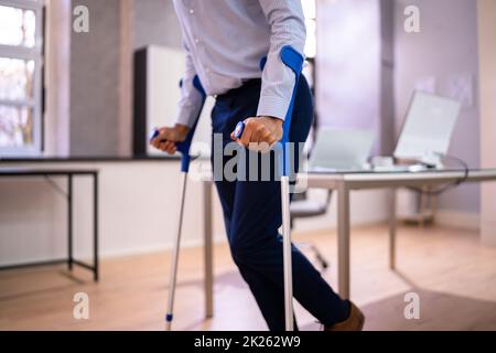 Arbeiter Mit Krücken Am Arbeitsplatz Oder Im Büro Stockfoto