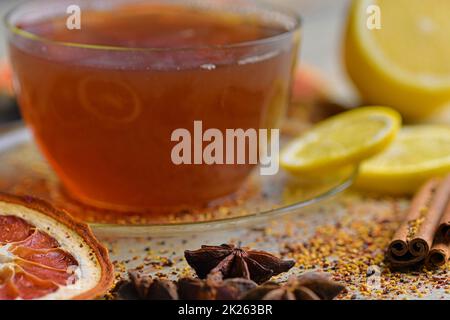 Eine Tasse Tee mit Zimtstangen auf einem Holztisch. Zimtstangen, Sternanis, Zitrone und getrocknete Früchte. Schwarzer Hintergrund. Makrobild. Stillleben-Konzept. Stockfoto