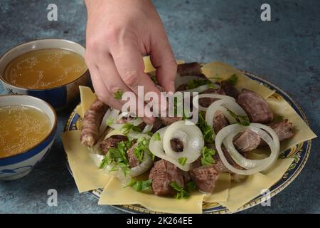 Beshbarmak – Kasachisches Nationalgericht, zubereitet mit Fleisch und Nudeln. Nahaufnahme des Schüssels Beshbarmak auf einem Teller auf dem Tisch. Große Stücke gedünstetes Fleisch und Zwiebeln Stockfoto