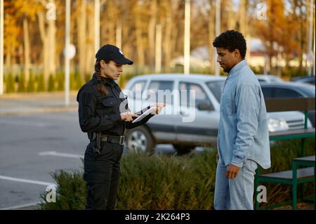 Weiblicher Polizist, der das Ausweisdokument der männlichen Passanten überprüft Stockfoto