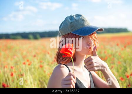 Lächelndes junges Mädchen mit einer Mohnblume, die den Daumen nach oben zeigt Stockfoto