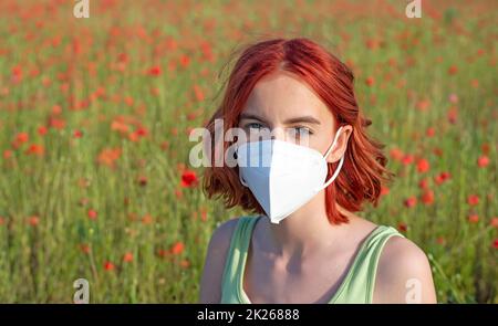 Frustriertes junges Mädchen mit Schutzmaske im Mohnfeld Stockfoto