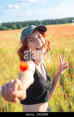 Glückliches junges Mädchen mit Mohnblume zeigt Siegeszeichen Stockfoto