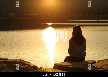 Weibliche Silhouette mit Blick auf den Sonnenuntergang in einem See Stockfoto