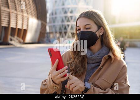 Junge Geschäftsfrau trägt KN95 FFP2 Maske mit Handy-App in der Stadt Straße Stockfoto