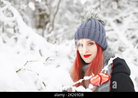 Wunderschönes rothaariges Mädchen, das im Winter mit zwei roten Herzen posiert. Stockfoto