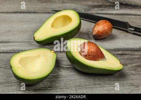 Zwei Avocados auf Holzbrettern Schreibtisch, zu halbieren, Samen sichtbar, Messer im Hintergrund. Stockfoto