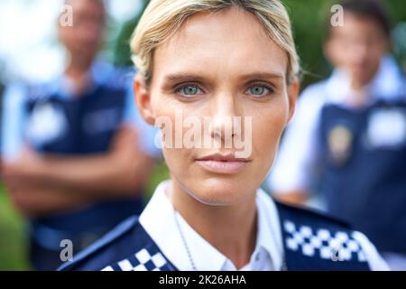 Den Frieden bewahren. Eine ernsthafte Polizistin mit ihren Kollegen im Hintergrund. Stockfoto