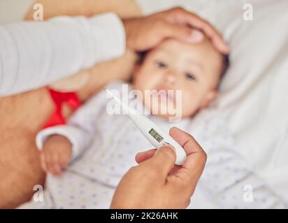 Thermometer, Spucke und krankes Baby im Bett mit der Hand der Eltern auf der Stirn, um zu Hause auf Fieber oder Grippe zu prüfen. Sorge, Fürsorge und Person, die sich um einen kümmert Stockfoto