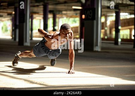 Seitenansicht eines muskulösen schwarzen Mannes in Sportkleidung, der während des Trainings auf der Straße der modernen Innenstadt mit städtischem Hintergrund Liegestütze macht Stockfoto