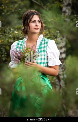 Frau in einem Dirndl mit einem Bouquet von Heidekräutern Stockfoto