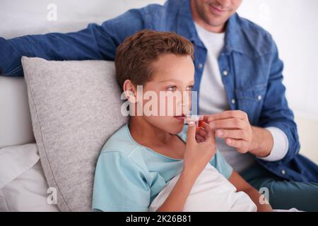 Ein fürsorglicher Vater, der seinem kranken kleinen Jungen zu Hause Medikamente gibt. Stockfoto