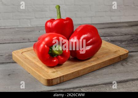 Ganze drei rote Paprika auf Schneidebrett Stockfoto
