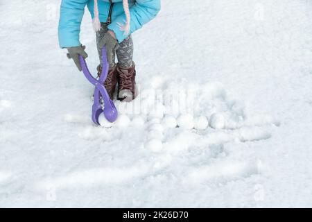 Das Kind hat Spaß beim Basteln von Schneebällen mit dem Spielzeugkunststoffautomaten. Kinder, die Schneebälle zwischen den Schneeverwehungen spielen. Platz für Text. Stockfoto