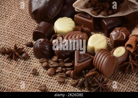 Auswahl an dunklen, weißen und Milchschokolade-Süßigkeiten, zefir (zephyr). Schokolade und Kaffeebohnen auf rustikalem Holzhintergrund. Gewürze, Zimt. Schokoladen-Hintergrund. Stockfoto
