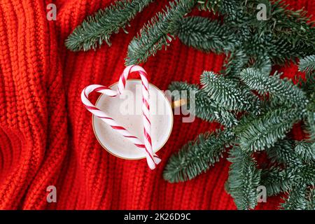 Weihnachtskomposition aus norwegischer Nobilis-Kiefer, dekoriert mit Lichtern und Zuckerstangen in Form eines Zuckerrohrs. Eine Tasse Cappuccino mit einem Zuckerrohr in Herzform. Weihnachtskonzept und Neujahrskonzept. Stockfoto