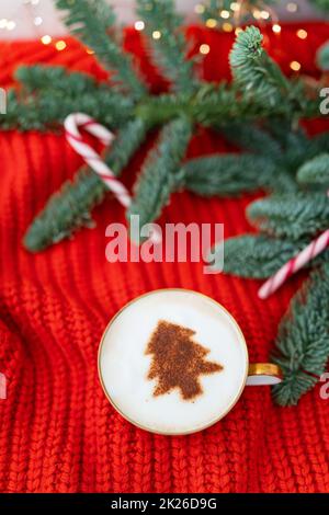 Weihnachtskomposition aus norwegischer Nobilis-Kiefer, dekoriert mit Lichtern und Zuckerstangen in Form eines Zuckerrohrs. Eine Tasse Cappuccino mit einem Weihnachtsbaummuster. Weihnachtskonzept und Neujahrskonzept. Stockfoto