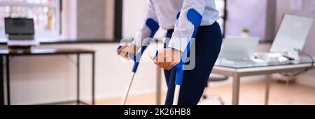 Arbeiter Mit Krücken Am Arbeitsplatz Oder Im Büro Stockfoto