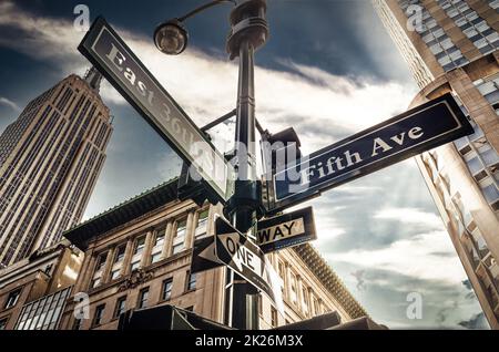 Fifth Ave 5th Ave, New York City-Schild, Blick aus dem niedrigen Winkel mit Sonnenuntergang und Empire State Building im Hintergrund, amerika, usa Stockfoto