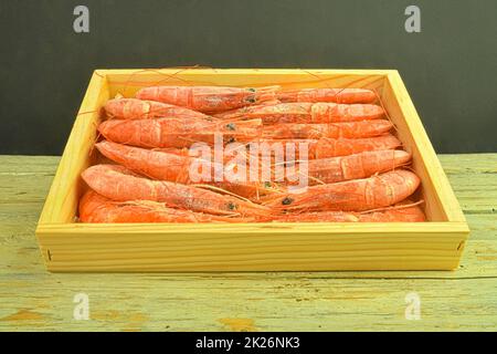 Rote Garnelen auf schwarzem und weißem Hintergrund in einer Holzkiste. Ansicht mit niedrigem Winkel und Kopierbereich. Meeresfrüchte Stockfoto