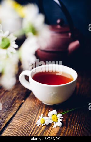 Tasse roten Tee und zwei Kamillenblüten Stockfoto