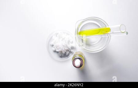 Meersalz in chemischer Uhrenglas und Nickelchlorid-Flüssigkeit in Reagenzglas neben Tropfflasche mit gelber Kosmetikflüssigkeit legen. Draufsicht Stockfoto