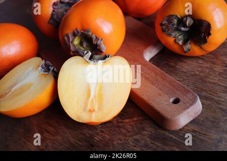 Frische Bio reife Kaki Früchte mit Scheibe auf alten Holztisch Hintergrund. Draufsicht. Flach liegend. Platz für Text und Inhalt kopieren Stockfoto