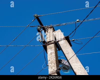 Betonmast mit elektrischen Drähten gegen den blauen Himmel. Stockfoto