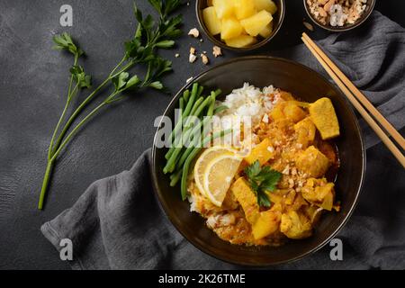 Ein Chicken Massaman Curry in schwarzer Schüssel auf dunklem Hintergrund. Massaman Curry ist das beste thailändische Gericht mit Hühnerfleisch, Kartoffeln, Zwiebeln und vielen Gewürzen, das von malaiischen und thailändischen muslimischen Kulturen beeinflusst wird. Stockfoto