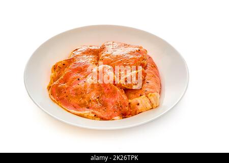 Schweinefleisch in Marinade liegt auf einem weißen Teller auf einem weißen isolierten Hintergrund Stockfoto