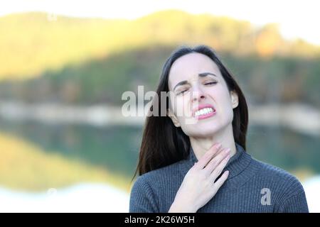 Frau mit Halsschmerzen, die sich in der Natur beklagt Stockfoto