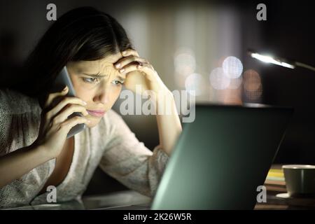 Besorgte Frau, die den Laptop überprüft und nachts telefoniert Stockfoto