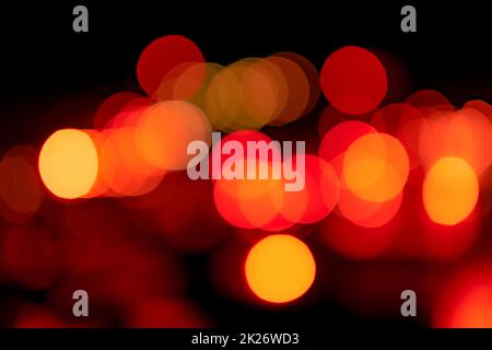 Verwischen Sie rotes und orangefarbenes Bokeh auf dunklem Hintergrund. Abstrakter Hintergrund des Stadtlichts. Bokeh-Licht mit kreisförmigem Bokeh. Rote und gelbe Anzeige auf Schwarz. Unscharfes Bokeh-Licht in der Stadt bei Nacht. Stockfoto