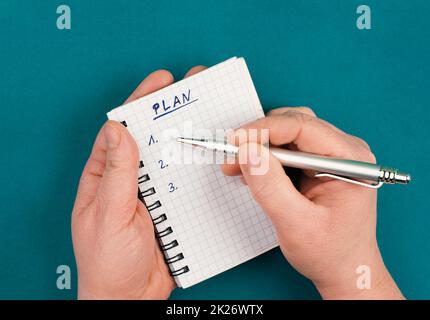 Leeres Notizbuch mit einem Stift auf einem petrolfarbenen Hintergrund, steht das Wort Plan oben auf der Seite und plant neue Ziele, To-Do-Liste Stockfoto