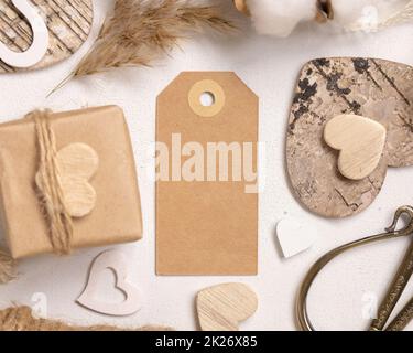 Leerer Geschenkanhänger zwischen Geschenk am Valentinstag, Draufsicht auf Herzen und getrocknete Blumen, russisches Label Mockup Stockfoto