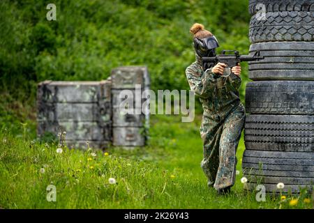 Junge Frau in Aktion beim Paintball spielen Stockfoto