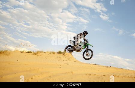 Professioneller Motocross-Fahrer, der den Sandberg hinunterrutscht Stockfoto