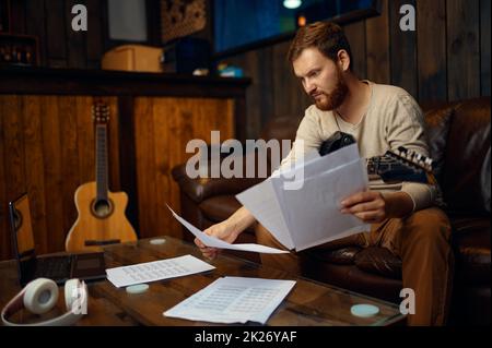 Junger Gitarrist, der beim Lesen von Musiknoten lernt Stockfoto