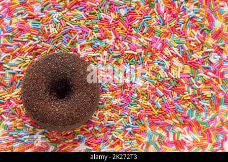 Köstlich aussehende Schokoladen-Donuts werden vor dem Hintergrund vieler heller Zuckergranulate platziert, die zum Beladen von Desserts und Eis in To verwendet werden Stockfoto