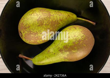 Zwei süße Birnen auf einer schwarzen Keramikplatte, Makro, Draufsicht. Stockfoto