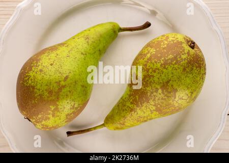 Zwei süße Birnen auf einer weißen Keramikplatte, Makro, Draufsicht. Stockfoto