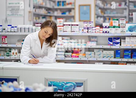 Sicherstellen, dass jede Verordnung korrekt ist. Aufnahme eines attraktiven jungen Apothekers, der an der Rezeptheke arbeitet. Stockfoto