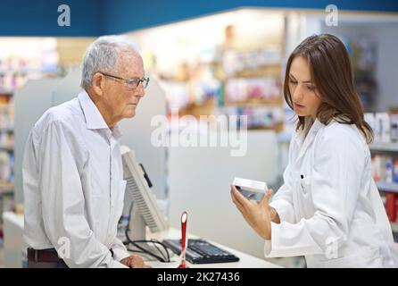 Füllen von Rezepten und Kundenbedürfnissen. Aufnahme eines jungen Apothekers, der einem älteren Kunden am Rezepturschalter hilft. Stockfoto