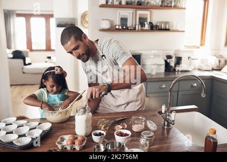 Backen Sie jemanden glücklich. Aufnahme eines Vaters, der seiner Tochter beibringt, wie man zu Hause in der Küche backen kann. Stockfoto