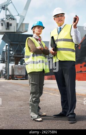 Eine effektive Kommunikation zwischen den Mitarbeitern ist von entscheidender Bedeutung. Zwei Ingenieure diskutieren auf der Werft über die Planung auf einem Gelände. Stockfoto