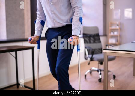 Arbeiter Mit Krücken Am Arbeitsplatz Oder Im Büro Stockfoto