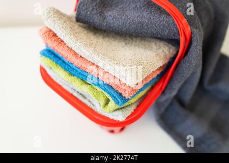 Bunte Handtücher liegen in einem roten Wäschekorb auf weißem Hintergrund. Wäsche waschen und bügeln, Draufsicht. Stockfoto