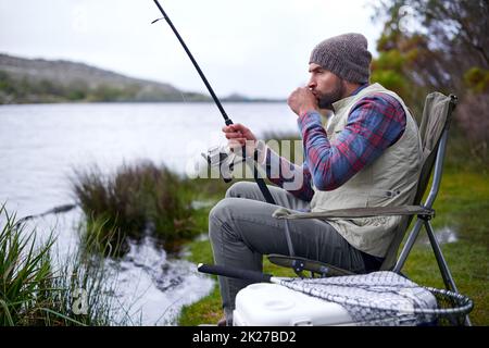 Es geht um Geduld. Ein gutaussehender Mann, der an einem natürlichen See angeln kann. Stockfoto