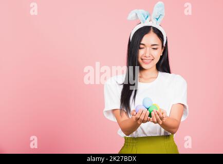 Lächelnde Frau mit Kaninchenohren und farbenfrohen Ostereiern als Geschenk an den Händen Stockfoto