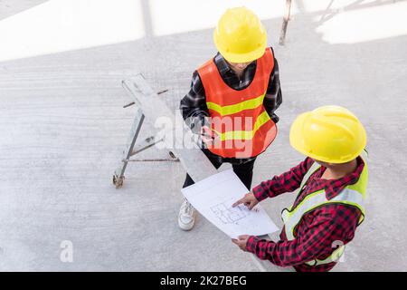 Der Architekt und der Kunde, der mit ihm spricht, helfen bei der Erstellung eines Plans mit dem Bauplan des Gebäudes auf dem Boden der Baustelle. Asiatischer Ingenieur Vorarbeiter, Mann und Frau, Meeting und Planung von Bauarbeiten, Draufsicht Stockfoto